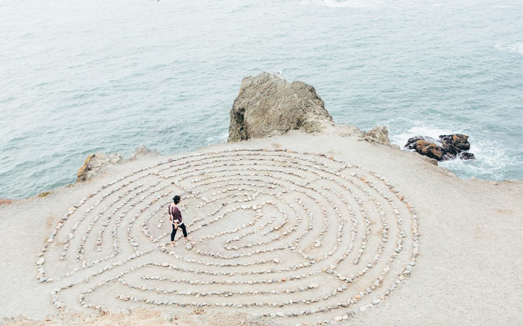 A man walking across a spiral labyrinth on the beach.